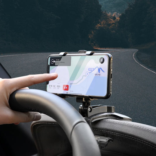 Hand holding a smartphone with a navigation app on a car dashboard, with a road and trees in the background.